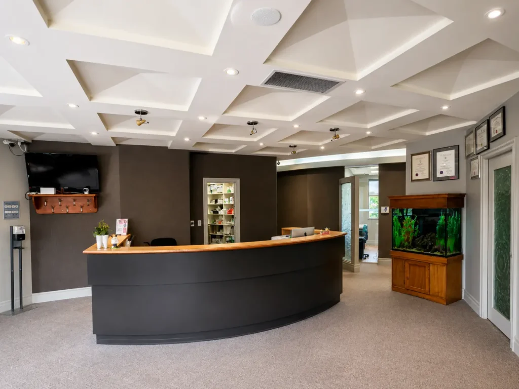 Curved wooden reception desk in a dental office lobby with coffered ceiling and recessed lighting