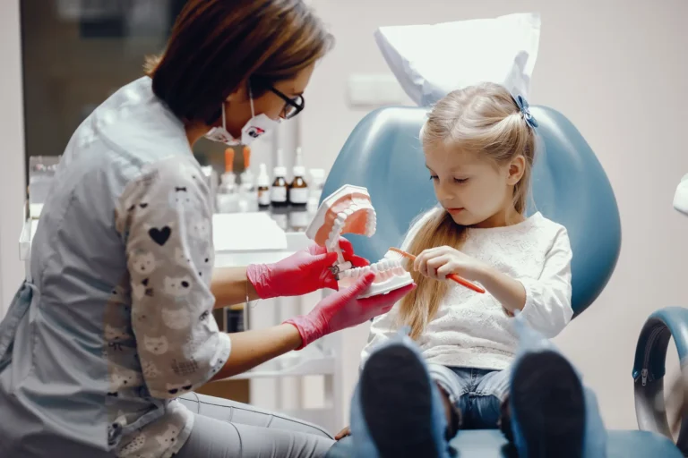 Female dentist treats a young girl in a dental chair with a tray of instruments nearby during a checkup