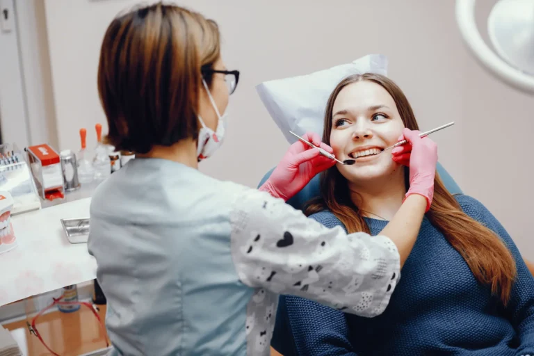 Gloved practitioner treats a reclining patient who wears a mouth retractor and smiles during a dental procedure
